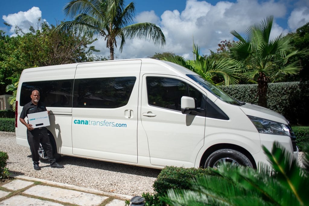 Cana Transfers driver holding a sign next to a white Toyota Hiace in Punta Cana